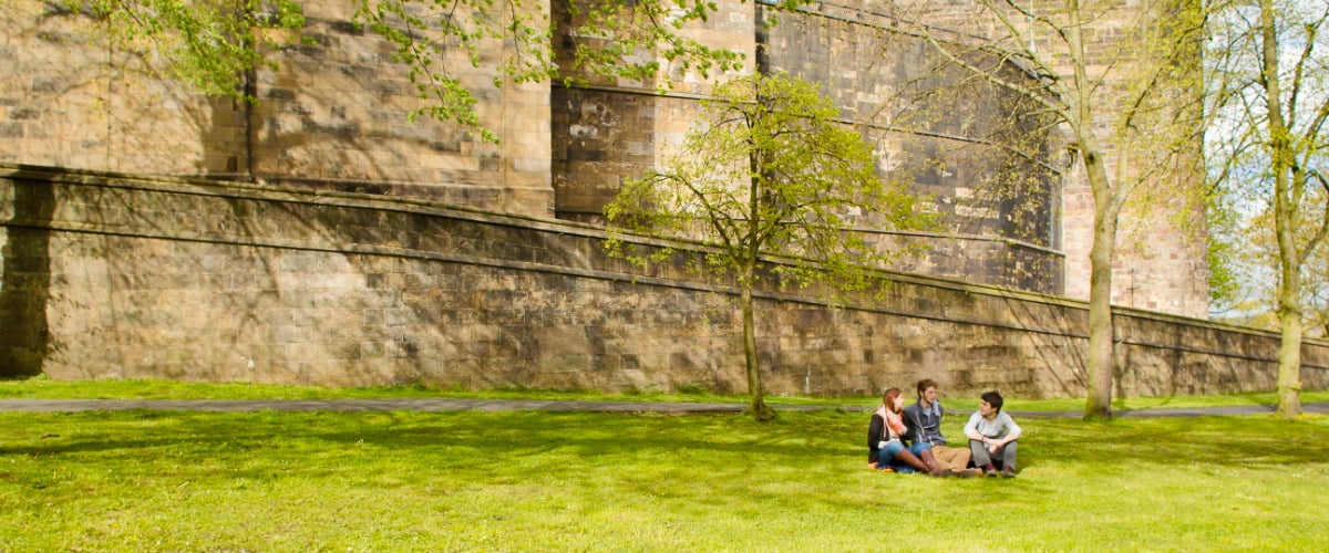 Three students sit on the grass in front of the ancient stone walls of 六合彩开奖结果 Castle.